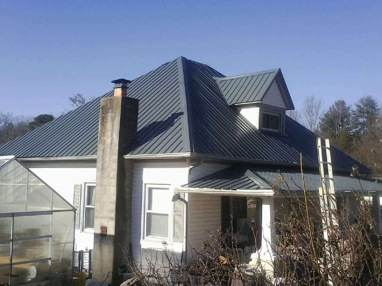 Dark blue standing seam metal roof on a white farmhouse with dormer — Slate & Tile Roof Repair by Roofing Brothers in Flovilla