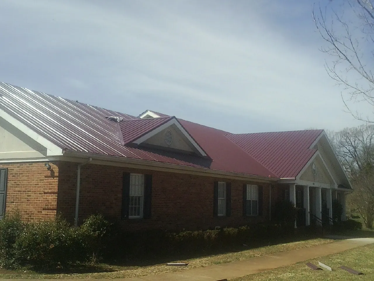 Red metal roof with gabled entries on a long brick building, from a Hail Damage Roof Repair job in Flovilla