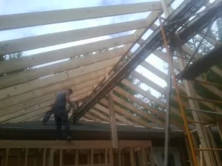 Rafters going up over a new addition with a worker on the wall in Flovilla