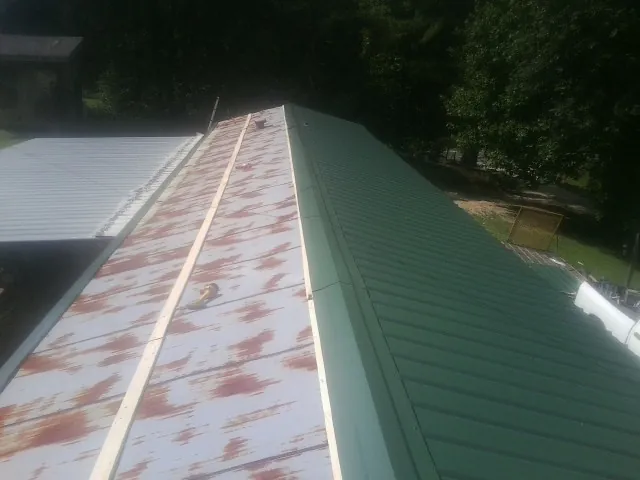 Old rusted panels beside newly installed green metal roofing — Wind Damage Roof Repair by Roofing Brothers in Flovilla