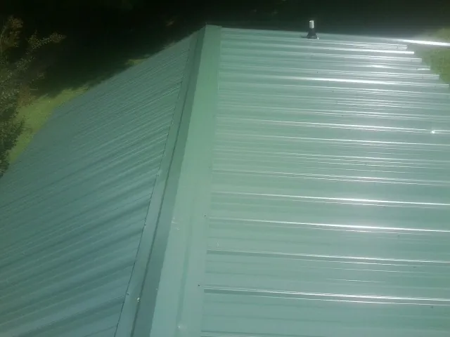 New green metal panels meeting at the ridge of a roof — Flat Roof Repair work by our crew in Flovilla