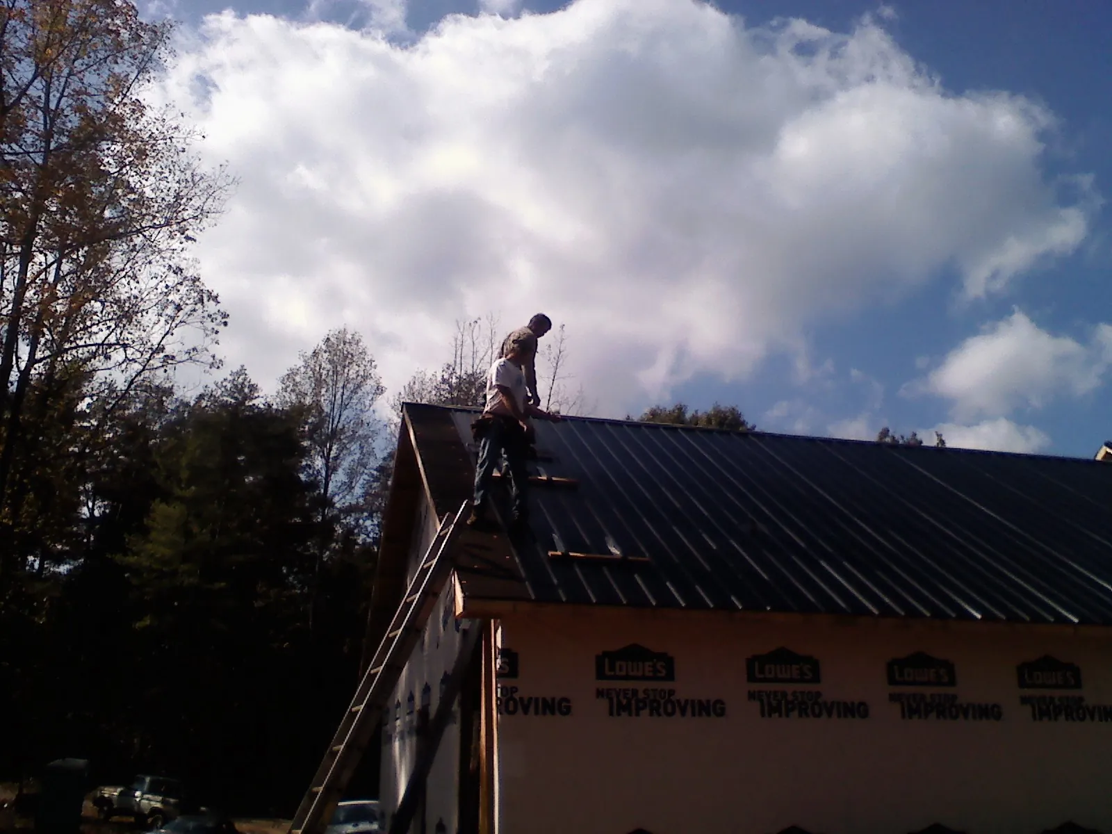 Roofer fastening dark metal panels high against a cloudy sky, from a Roof Inspection job in Flovilla