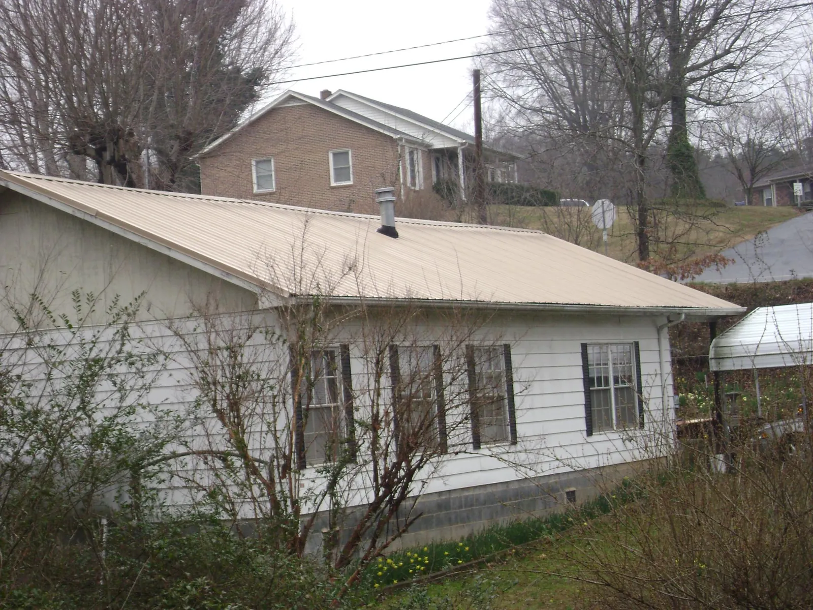 Tan metal roof on a white sided house set into a hillside — Commercial Roofing by Roofing Brothers in Flovilla
